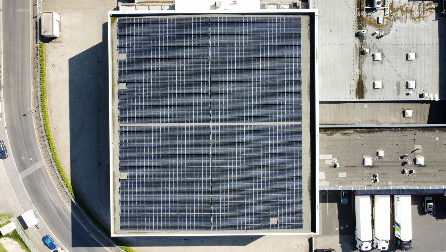 Gewerbehalle mit großflächiger Photovoltaikanlage auf dem Flachdach, Drohnenaufnahme von oben