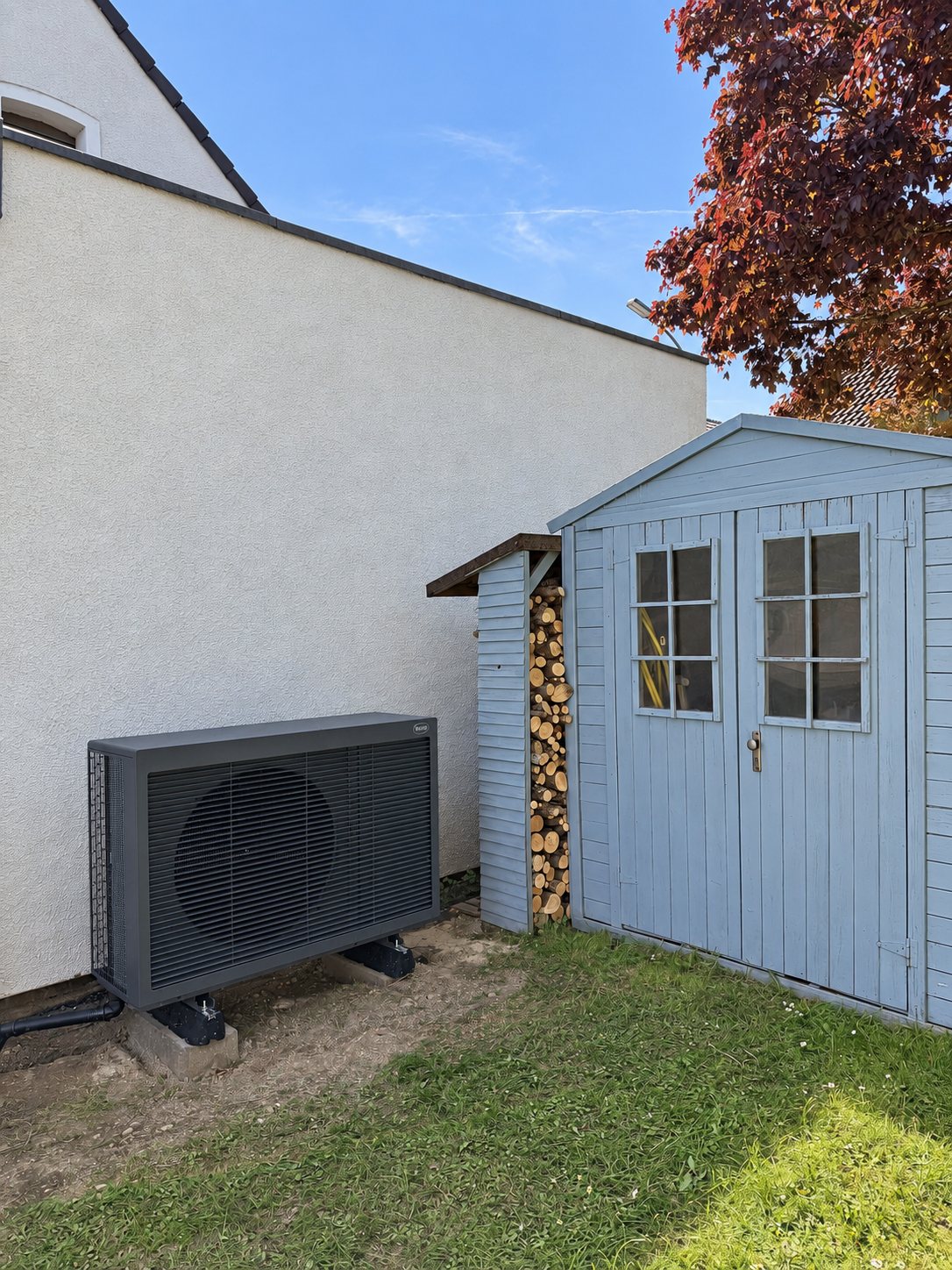 Wärmepumpe mit Holzverkleidung neben einem Gartenhaus