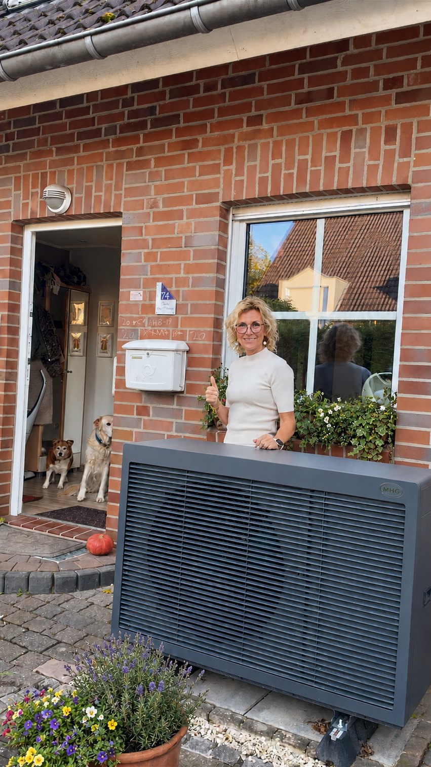 Kundin mit Daumen hoch neben der neuen MHG-Wärmepumpe vor ihrem Klinkerhaus